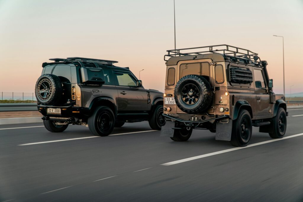 Two Land Rover Defenders drive on a highway in Erbil, Iraq during sunset, showcasing urban adventure.